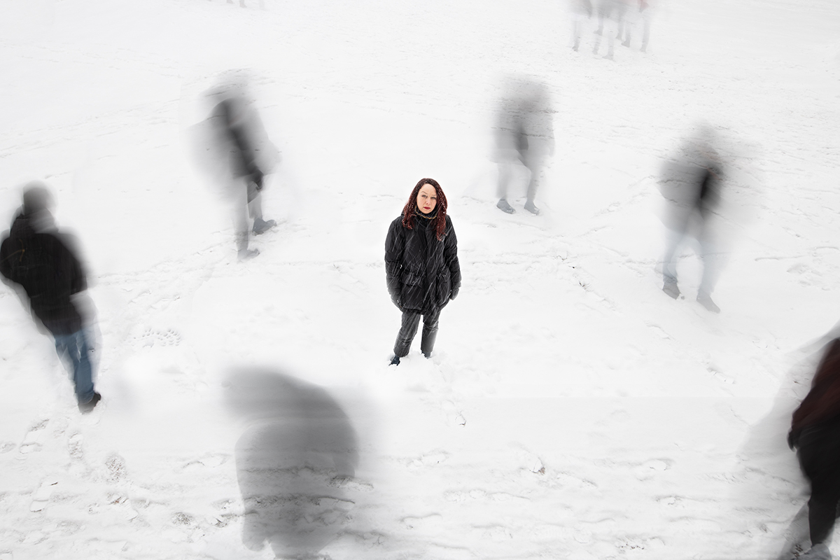 En kvinne står i snoen med skygger av mennesker rundt seg. Fotografi.